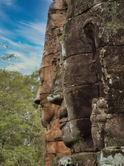 Khmer Smiling Stone Face - A close-up of a weathered, smiling stone face carving on a historic temple at Angkor, with detailed features and textures.