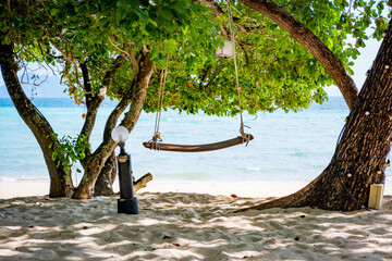 Wooden swing inviting relaxation under a shady tree on a pristine white sand beach, enjoying the tranquil turquoise ocean view in Koh Kradan, Thailand