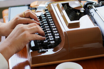 Close-up of hands typing on a vintage brown typewriter, symbolizing retro communication, writing, and creativity.