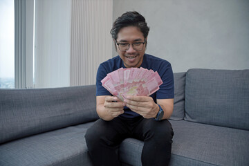 Asian young man holding Rupiah banknotes showing fist appreciating the joy of getting money. THR