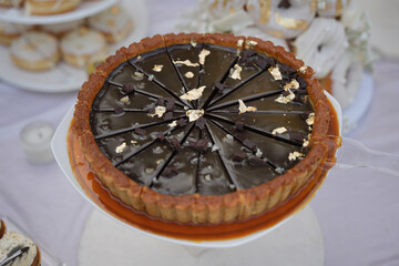 Chocolate pie topped with gold flakes and chocolate chunks is neatly sliced and displayed at a dessert table