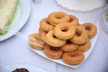 A stack of plain donuts is neatly arranged on a white square plate and displayed on the dessert table.