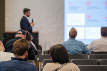Fototapeta premium Business seminar with presenter delivering talk while attendees listen and view bright slides on large screen in modern conference room