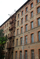 Schio, VI, Italy - September 22, 2025: Deatil of industrial Building called FABBRICA ALTA with long solid iron fire escape stairs on the exterior of an old century-old building with red face-brick