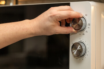 Human hand operating the control panel of a white microwave, adjusting settings for food preparation.