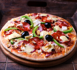 Pizza with chorizo ​​sausage, mozzarella cheese, green pepper and black olives. Rustic wooden background. Soft focus.	