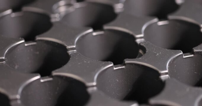 an empty plastic container with a large number of round holes for growing seedlings, a black plastic tray for seedlings