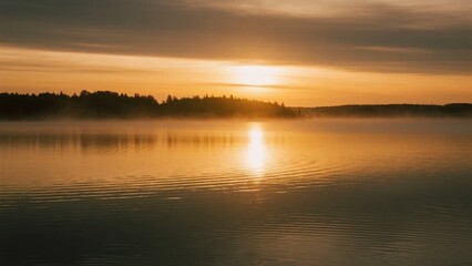Fototapeta premium Sunrise over a calm lake with mist rising from the water and trees in the distance