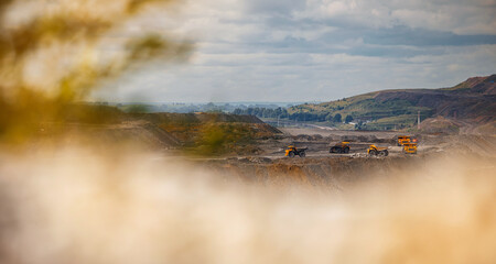 Expansive view of open pit coal mine with heavy machinery under cloudy sky, sunlight