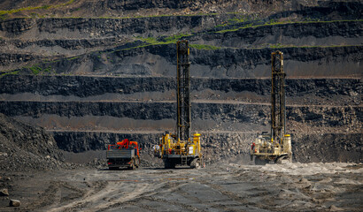 Massive open pit coal mine with heavy drill machinery and layered terrain