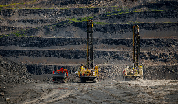 Massive open pit coal mine with heavy drill machinery and layered terrain