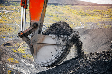 Excavator digging coal in large open pit mine landscape