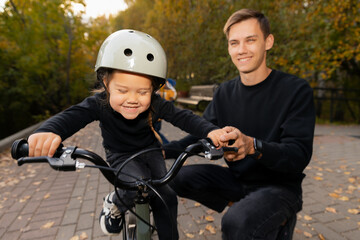 Obraz premium Dad and daughter learning with ride on bicycle for teaching at outdoor park with sunlight. Happy moments of life, lifestyle of fatherhood.