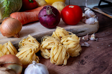 Dry Italian Tagliatelle pasta on a kitchen work top together with various vegetables.