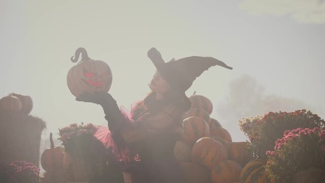 unrecognizable dark silhouette beauty young woman witch with orange pumpkin carved Jack o Lantern in foge smoke. fantasy girl, dress black hat. Halloween holiday harvest pumpkins Thanksgiving Day 4k