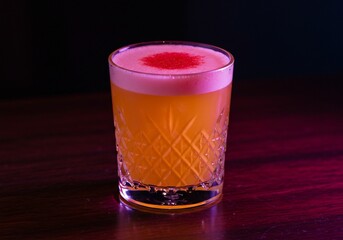 Neon-Lit Orange Sour Cocktail with Crimson-Dusted Pink Foam in a Crystal Glass