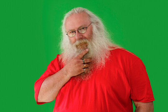Man dressed as Santa Claus poses thoughtfully against a green screen background, wearing glasses and a red shirt