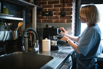 Person Using Espresso Machine in Modern Kitchen With Stainless Steel Sink and Brick Wall