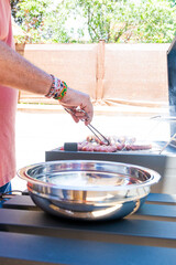Vertical image of a man cooking on a BBQ who is removing from the grill the sausages he is preparing and ready to eat. He is removing the sausages and placing them in an aluminum dish, to take them to