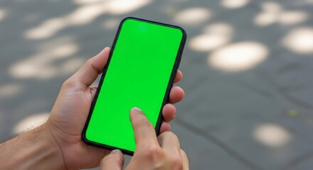 Person holding smartphone with green screen outdoors, tapping the display.