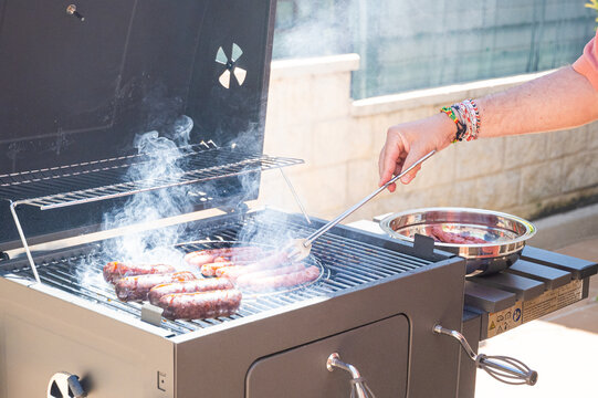 Arm of a man watching the steaming meat he is cooking on his barbecue grill.