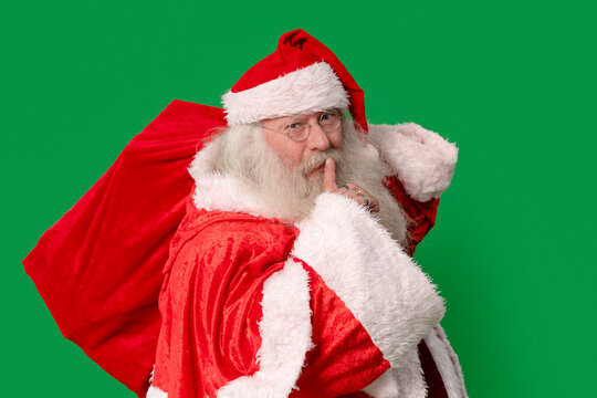 Santa Claus, carrying a large sack, asks everyone to be quiet, set against a vibrant green background