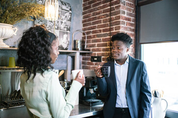Man In Suit And Woman In Light Jacket Sharing Coffee In Cozy Cafe