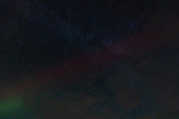 A dark sky filled with countless stars and faint aurora bands, partially covered by drifting clouds, creating a moody and mysterious celestial scene.