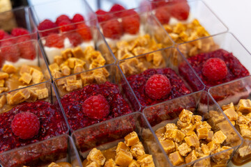 Mini raspberry and caramel dessert cups close-up. Close-up of elegant dessert cups filled with raspberry compote, caramel chunks, and cream, arranged in neat rows for catering or events.