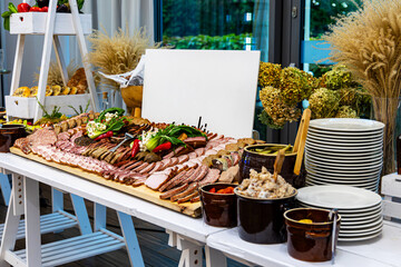 Traditional cold cuts buffet with rustic side dishes. Beautifully arranged buffet table featuring sliced cold cuts, sausages, pates, pickles, and rustic spreads in a festive setting.