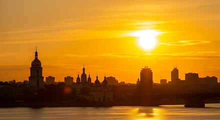 Obraz premium Golden sunset over a city skyline with architectural silhouettes reflecting on water.