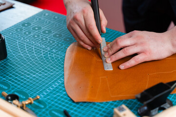 Artisans trim edges and prepare genuine leather. Cutting leather with knife and ruler. The artisan...