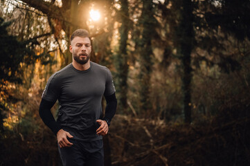 Determined male athlete running in forest at sunset