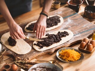 Hands spread poppy seed filling on dough for holiday sweet bread like Cozonac or Babka. The preparation process on a wooden board with other ingredients ready for baking