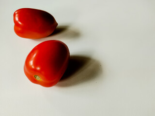 Two ripe red tomatoes are placed on a smooth, white surface.