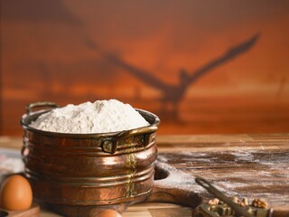 On a rustic wooden surface, baking begins. Flour is piled high in a copper pot, with eggs nearby. Walnuts and a nutcracker wait, ready to be added to the Cozonac