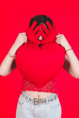 Young woman plays with a heart shaped cushion, she makes cheerful expressions towards the camera, Valentine's Day concept.