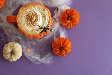 Halloween themed flat lay with a pumpkin latte, decorative pumpkins and spiderwebs on a purple background.