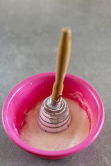 Whipped egg white in pink bowl with wooden whisk on kitchen counter