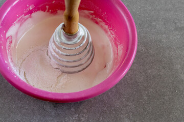 Whipped egg white with powdered sugar in pink bowl on kitchen counter.