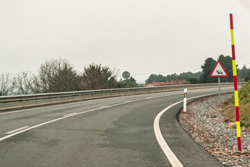 Vertical sign with a triangle with red border and white background indicates danger due to the proximity of a section with traffic jams or traffic jams. The sign is seen on a curved road. 
