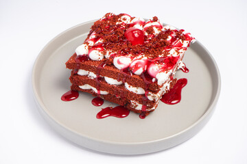 Layered cake slice with cream, red syrup, cherries, and crumbs on ceramic plate over dark surface, top view food photography for dessert presentation
