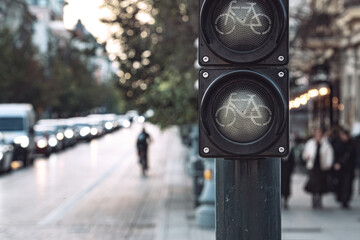 Close-up of turned off bicycle traffic light signal illuminated on busy city street with cyclists and pedestrians commuting during daytime
