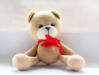 Handmade knitted bear toy with beige body and brown spots. Perfect for crafts, children's toys and unique gifts.. teddy bear with red ribbon