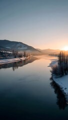 Beautiful winter sunrise over a serene river with snow covered banks and trees reflecting the golden sky
