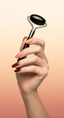 A female hand with a stylish autumn gradient manicure holds a black obsidian face roller. Skincare tool for facial massage and anti-aging spa treatments. Concept of beauty, wellness, and self-care.