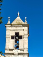 An old bell tower with a clock against the background of a bright blue sky.