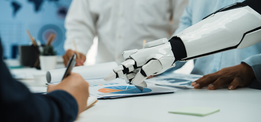 A robotic arm aids a business team in analyzing data and preparing reports, showcasing the integration of advanced technology in a collaborative office setting.Noogenesis