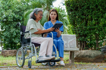 Caregiver provides assistance and support to senior in wheelchair, sharing information on tablet in serene outdoor setting. This moment highlights importance of care and companionship