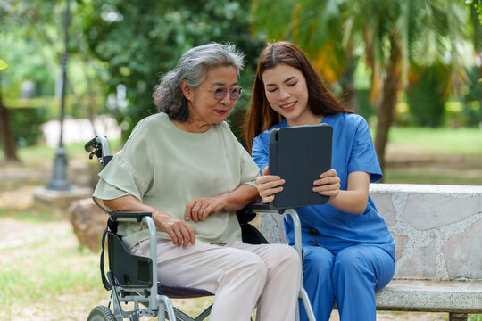 Caring caregiver provides assistance and support to senior in wheelchair while using tablet outdoors, showcasing importance of companionship in care